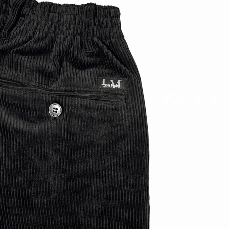 Nahaufnahme von schwarzem Cordstoff, einer Gesäßtasche mit Knopf und dem elastischen Bund der Hose
