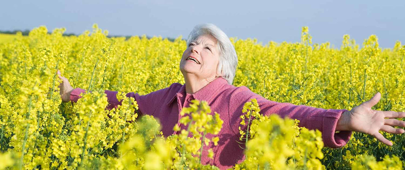 Ældre kvinde nyder en gåtur i en gul blomstermark for Seniorshop.dk