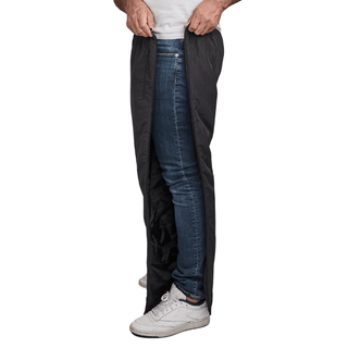 Mann öffnet schwarze Dobsom Thermohose seitlich über blauen Jeans und weißen Turnschuhen